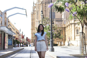 Fototapeta premium Young woman, natural, with brown hair, light blue shirt and linen pants, walking and observing the wonders of the city while on vacation. Concept naturalness, simplicity, travel, vacation.