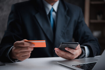 Businessman in suit holding credit card, making online payment with smartphone. Represents digital finance, secure transactions, e-commerce. Ideal for financial services, online banking.