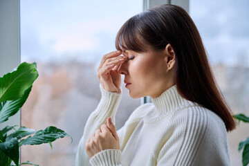 Obraz premium Middle aged woman experiencing headache migraine, at home near window
