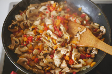 Top view of a frying pan with vegetables being fried on the stove, close-up of the process of preparing a vegetarian dish, steam rising above the vegetables