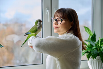Middle aged woman and parrot together at home, near winter window © Valerii Honcharuk