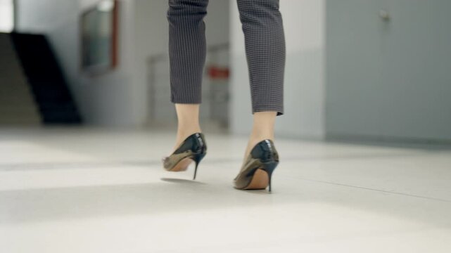A woman wearing high heels walks down a hallway. Concept of elegance and sophistication, as the woman's attire and posture suggest that she is attending a formal event or going to work