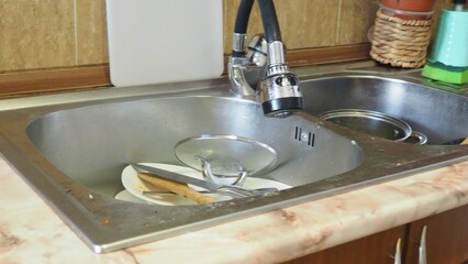 dirty dishes in the sink, plates, pans, lids. dishwashing liquid. female hands washing dirty dish holding soap foam sponge in the kitchen