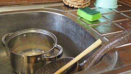 dirty dishes in the sink, plates, pans, lids. dishwashing liquid. female hands washing dirty dish holding soap foam sponge in the kitchen