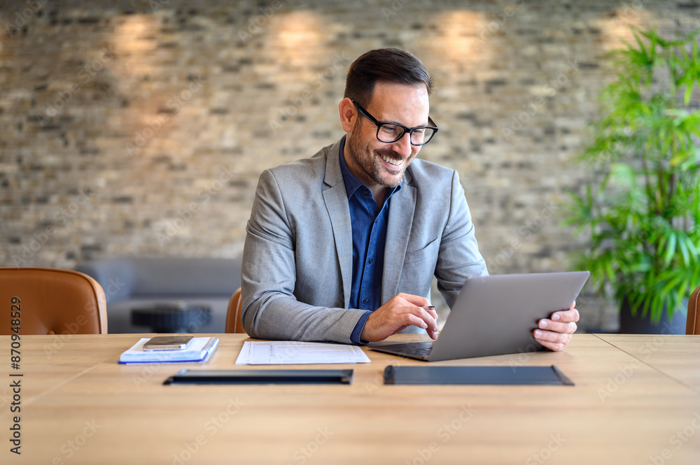 Wall mural handsome it engineer in eyeglasses smiling and developing website over laptop on desk in modern offi