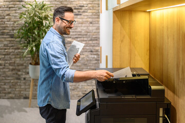 Side view of happy financial advisor putting documents in printer and making photocopies in office