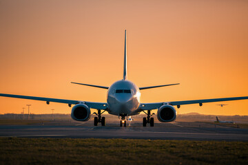Traffic at airport at golden sunset. Front view of taxiing airplane while other taking off from the runway..