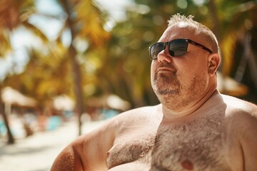 Fat man in swimsuit and sunglasses on blured beach background with palm. ai generative