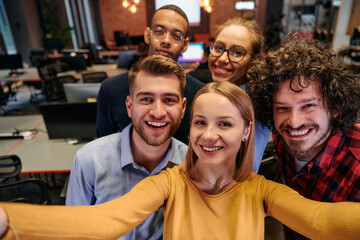 A diverse group of business professionals take a break from their tasks in a modern startup office to capture a creative selfie, showcasing teamwork and a vibrant workplace culture