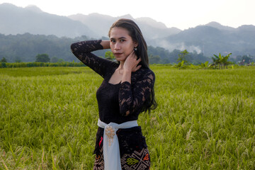 a beautiful Indonesian woman wearing a black Balinese kebaya with a background of rice fields and mountains