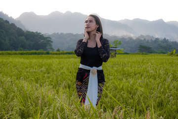 a beautiful Indonesian woman wearing a black Balinese kebaya with a background of rice fields and mountains