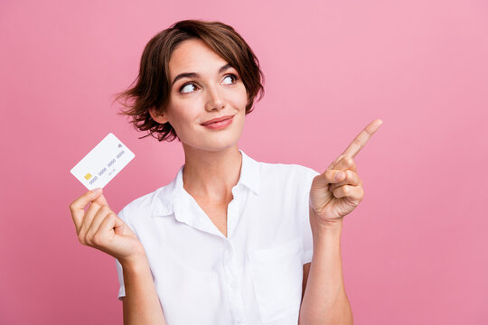 Portrait of optimistic woman wear stylish blouse holding debit card directing look at offer empty space isolated on pink color background