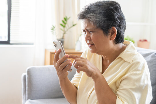 Presbyopia, Hyperopia mature, aged asian woman having vision problem trying to stare text on smart mobile phone screen on sofa at home, eye disease of elderly. Poor eyesight farsightedness concept.