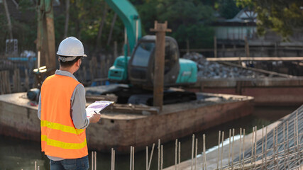 Fototapeta premium Construction engineer working on a bridge construction site over a river,Civil engineer supervising work,Foreman inspects work at a construction site