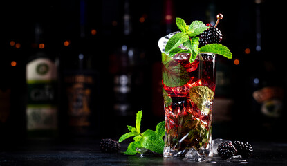 Summer blackberry low alcohol cocktail with rum, tonic, mint and ice, black background with bottles