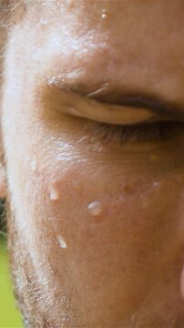 Epic extreme close-up shot of sweaty man outdoor in park. Drop of water on his face macro slow motion. Turning head from dowm to camera Vertical shot.