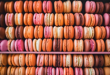 A close-up view of a large assortment of colorful macarons in various pastel shades, including pink, green, and orange, arranged in a visually appealing manner.