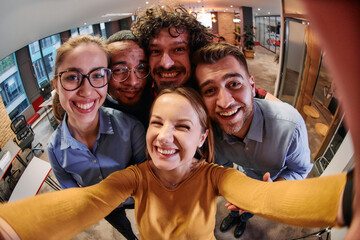 A diverse group of business professionals take a break from their tasks in a modern startup office to capture a creative selfie, showcasing teamwork and a vibrant workplace culture