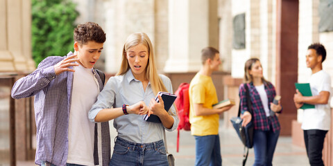 Fototapeta premium Shocked students in university campus looking at watches, being late for classes, copy space
