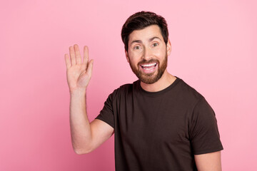 Fototapeta premium Portrait of cheerful pleasant man with bristle stylish hairdo wear brown shirt waving palm say hi isolated on pink color background
