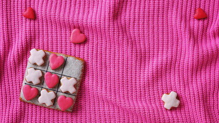 Noughts and crosses. A web banner for a website on the theme of love. Gingerbread on a pink sweater background. Horizontal Wallpaper