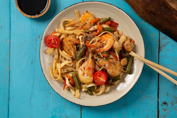 shrimp and udon vegetables pad thai sauce and chopsticks and soy sauce on a blue table. copy space