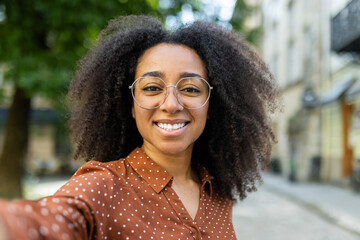 Smiling woman with glasses taking a selfie outdoors on a sunny day
