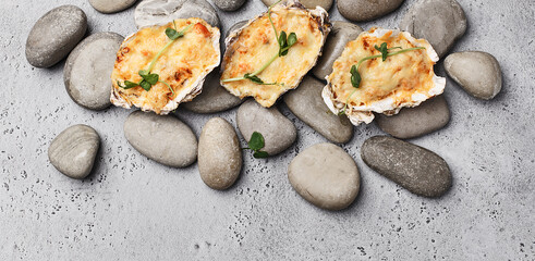 Baked stuffed oysters decorated with micro greens, served on stones over gray concrete background....
