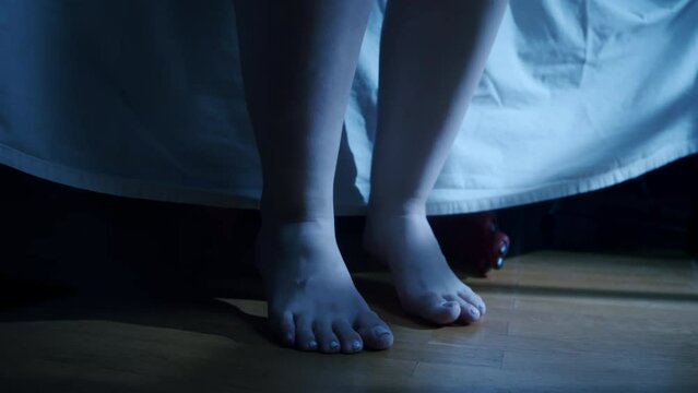 Scary monster under bed want to grabbing teen girl by legs, close up. Demon creepy hands reaching out from underneath the bed, coming out from under a bed to grab. Horror concept. Halloween nightmare