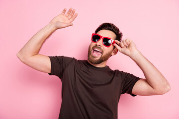 Photo of positive man with stylish bristle dressed brown t-shirt touch sunglass dancing in night club isolated on pink color background