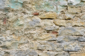 Background of a natural stone or sandstone masonry wall with cement in South France. Detailed stone texture image in beige, brown, grey and green