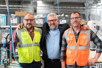 Group portrait of three distribution warehouse workers team working together, arms crossed and looking at the camera in work overalls.