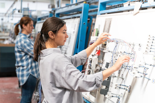 Young adult females technicians in a work wear is working on manufacturing of home appliances factory an electrical control panel.