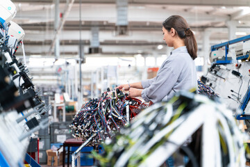 Women in a production line is working on a machine in a auto cable factory. There are many colorful wires in the foreground and background.