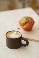 Cappuccino and cruffin, on the coffee shop table. Minimalist style. Coffee shop lifestyle. Black ceramic cup.