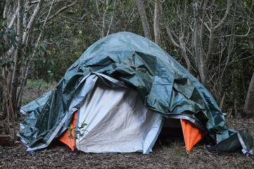 Orange tent covered with green tarp under trees © Nataly Regina