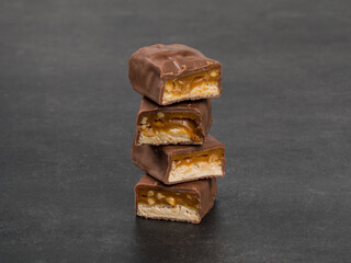 Candy bar with nougat, caramel, peanuts and hazelnuts. In chocolate. Close-up. Dark background