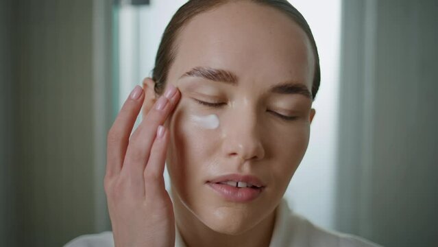 Beauty model applying cream under eyes closeup. Pretty girl moisturizing skin