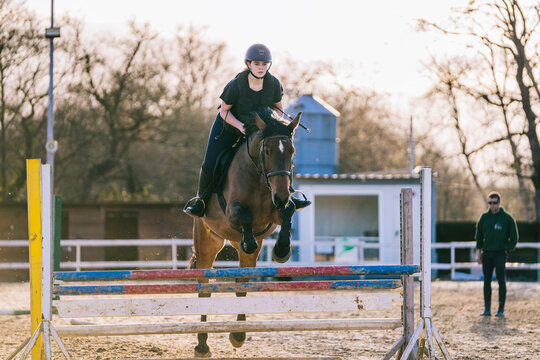 Serious lady with horse negotiating parallel oxer