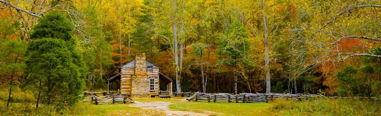 a restored log cabin surrounded by trees showing fall colors and a split rail fence, in the Cades...
