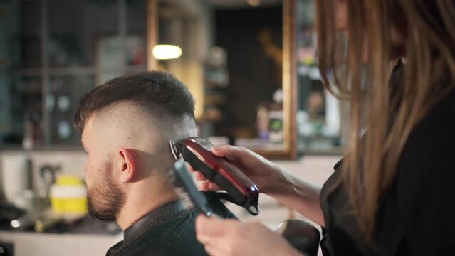 Young female barber making men's undercut haircut hairstyle using Haircut Clipper in Modern style barber shop. Haircare service local small business, cosmetics and personal care industry 4K video