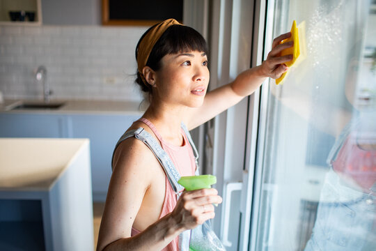 Asian woman cleaning window with spray and sponge