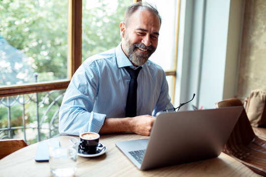 Smiling middle aged businessman having video call on laptop at cafe