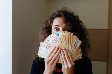 surprised woman watching behind her face behind money cash looking at camera