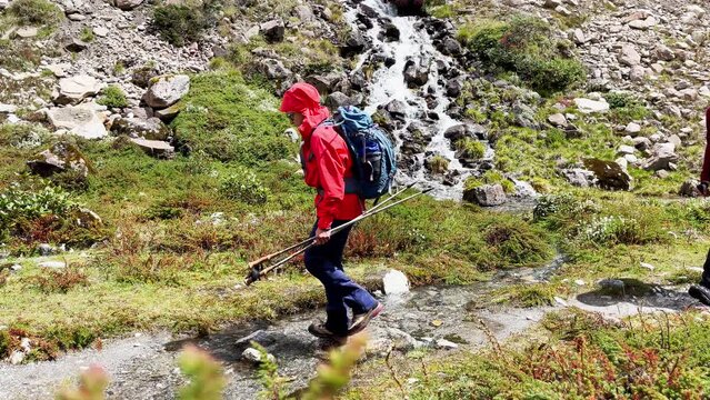 Trekkers couple backpackers with trekking poles slow motion crossing Mountain creek running down in Makalu Barun National Park near Kothe settlement. Mera peak climbing route, Himalayas, Nepal.
