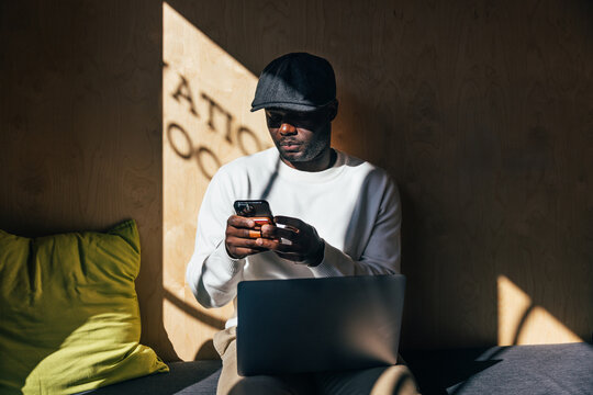 African American man using smartphone and laptop indoors