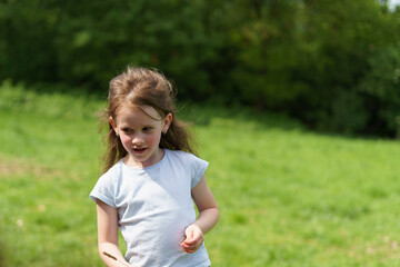 Smiling little cute preschooler girl on a green clearing in the forest. Happy childhood concept...