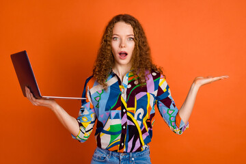 Photo of impressed speechless staring confused girl wear trendy print clothes hold netbook empty space isolated on orange color background
