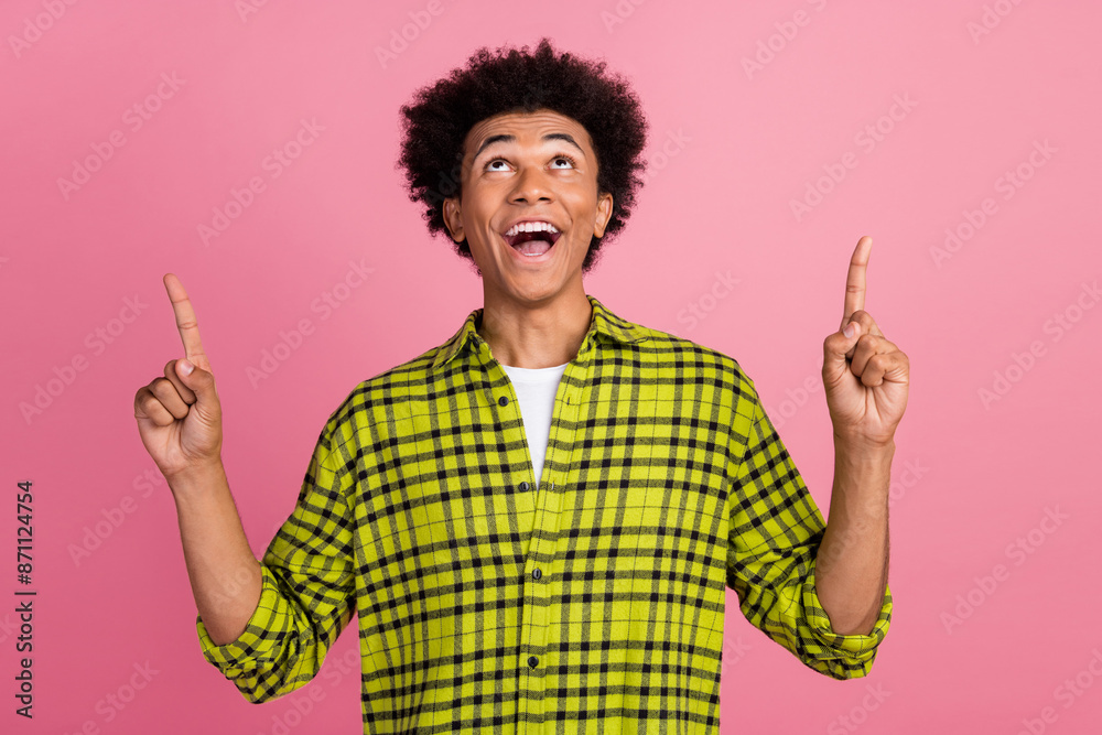 Poster photo of nice young man point fingers up empty space wear shirt isolated on pink color background