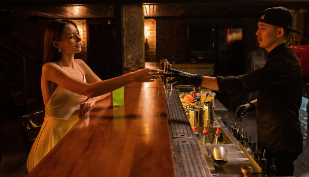 Young woman in dress paying for cocktail at the bar 